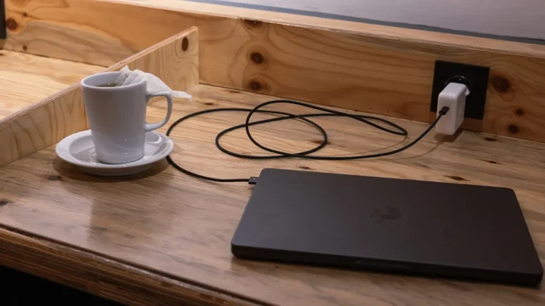 Ahşap masada şarjda duran kapalı bir laptop ve yanında bir fincan çay